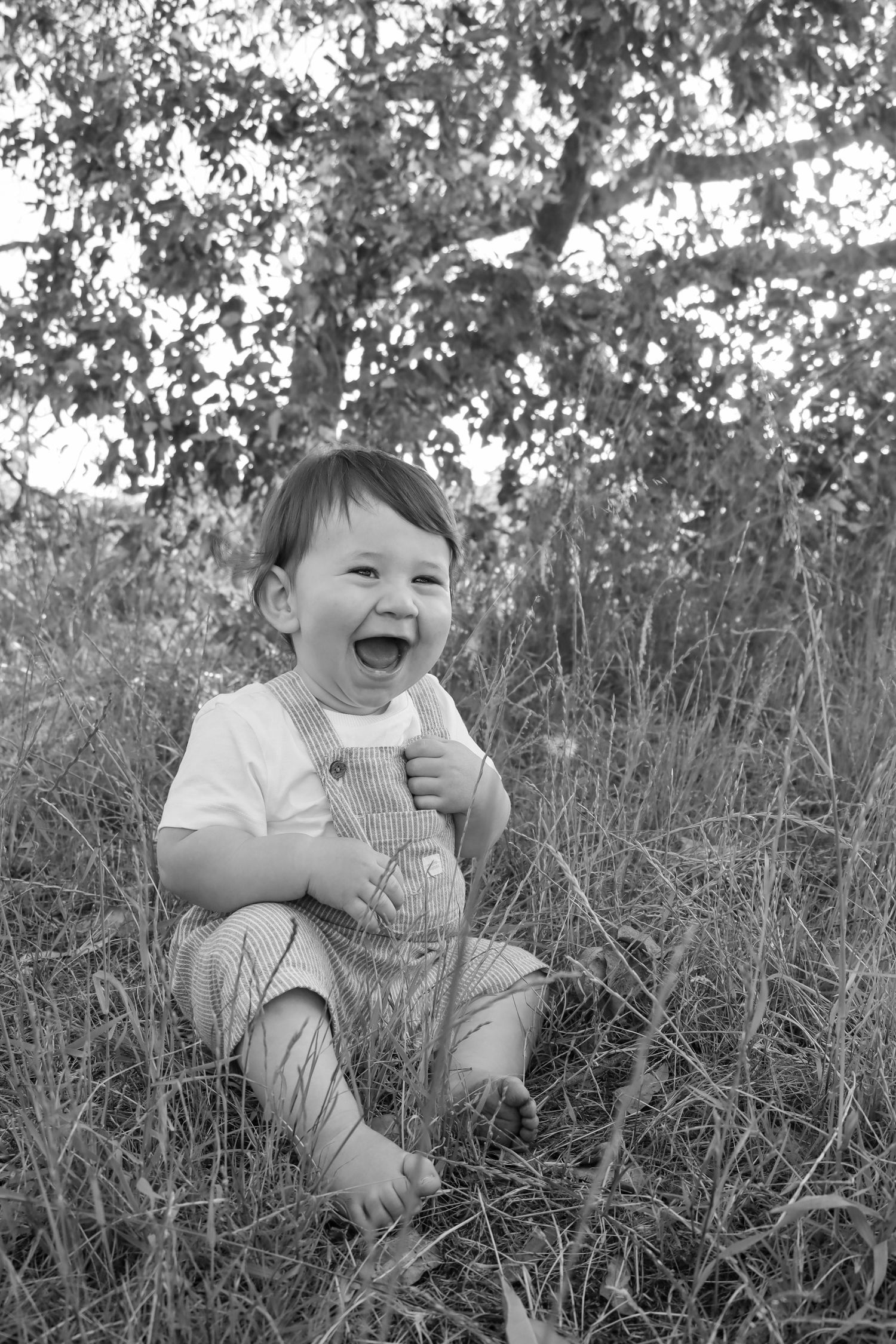 Baby laughing in a field at sunset during a candid family photography session.