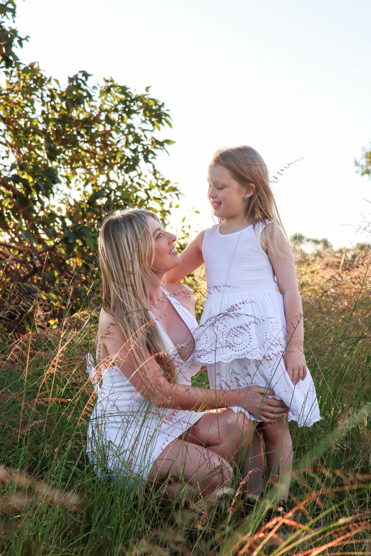 Mum and daughter connection in a field at sunset during a candid family photography session.