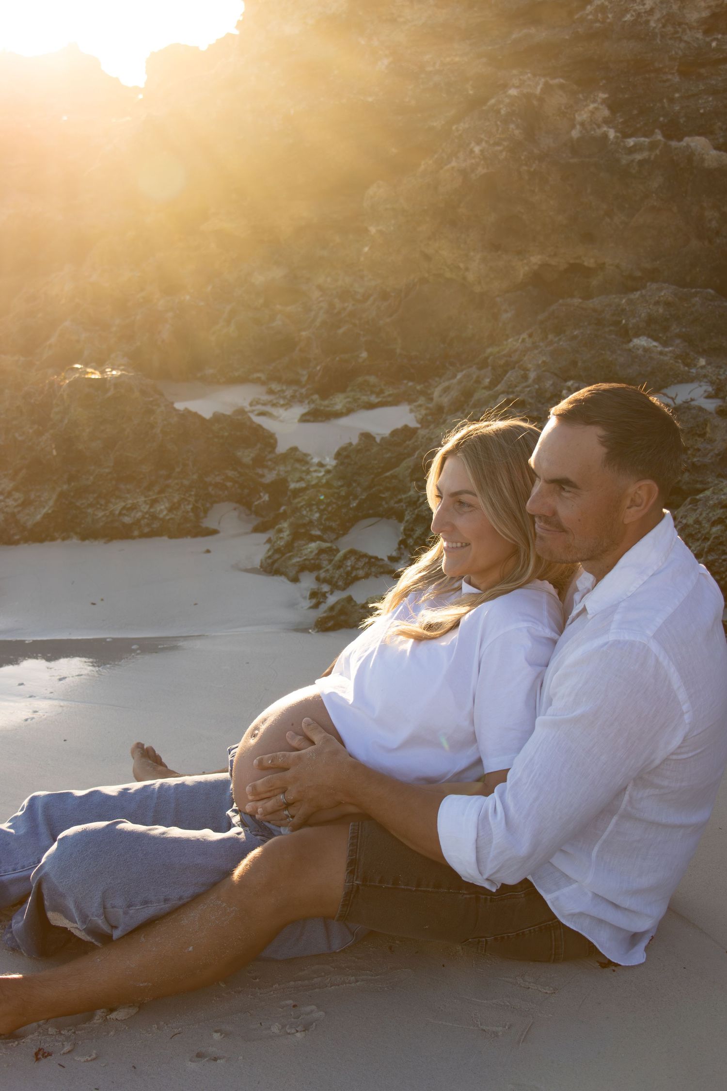 Couple celebrating their pregnancy announcement with natural, candid photos at a Perth beach during golden hour.