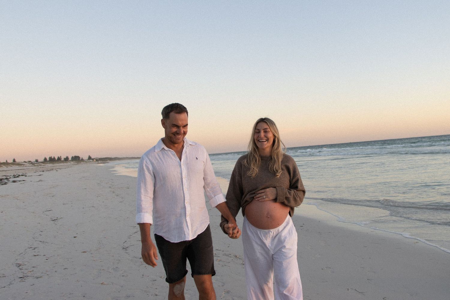 Mum-to-be walking along the beach with her partner during a natural outdoor maternity photography session in Perth at sunset.