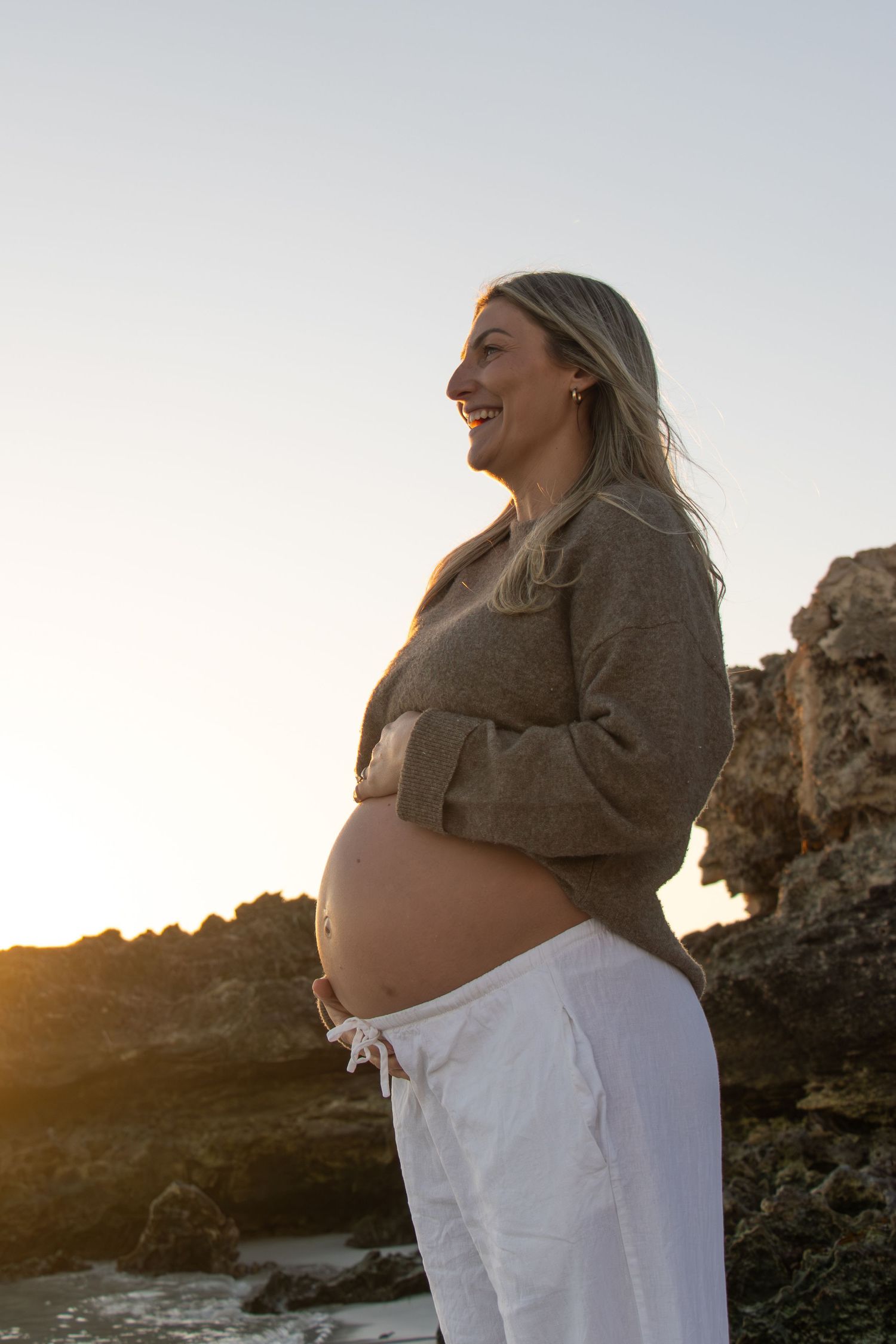 Expecting mum holding her baby bump while smiling at her partner during a relaxed outdoor maternity session in Perth.