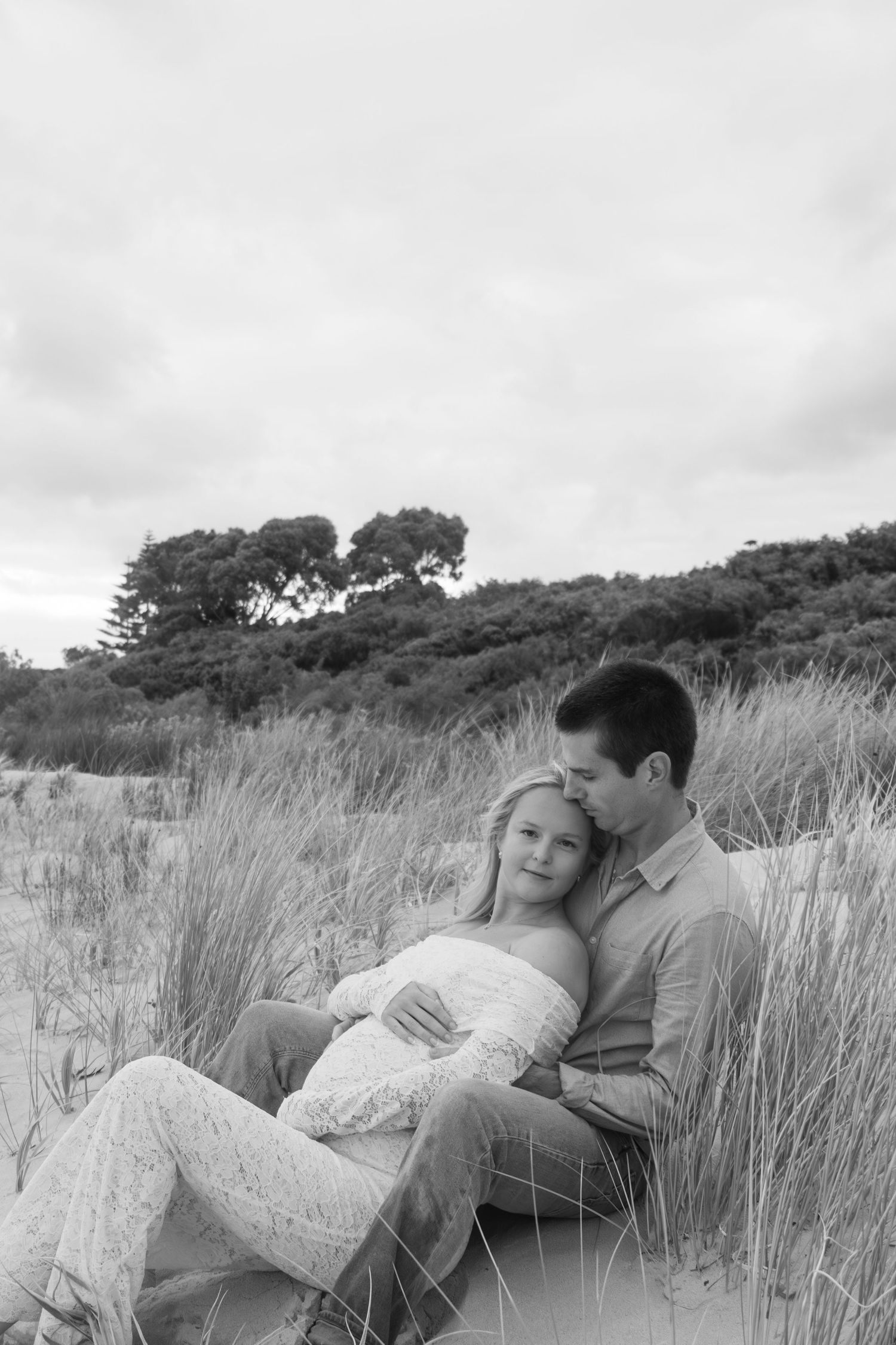 Expecting mum holding her baby bump while smiling at the camera during a relaxed outdoor maternity session in Albany.