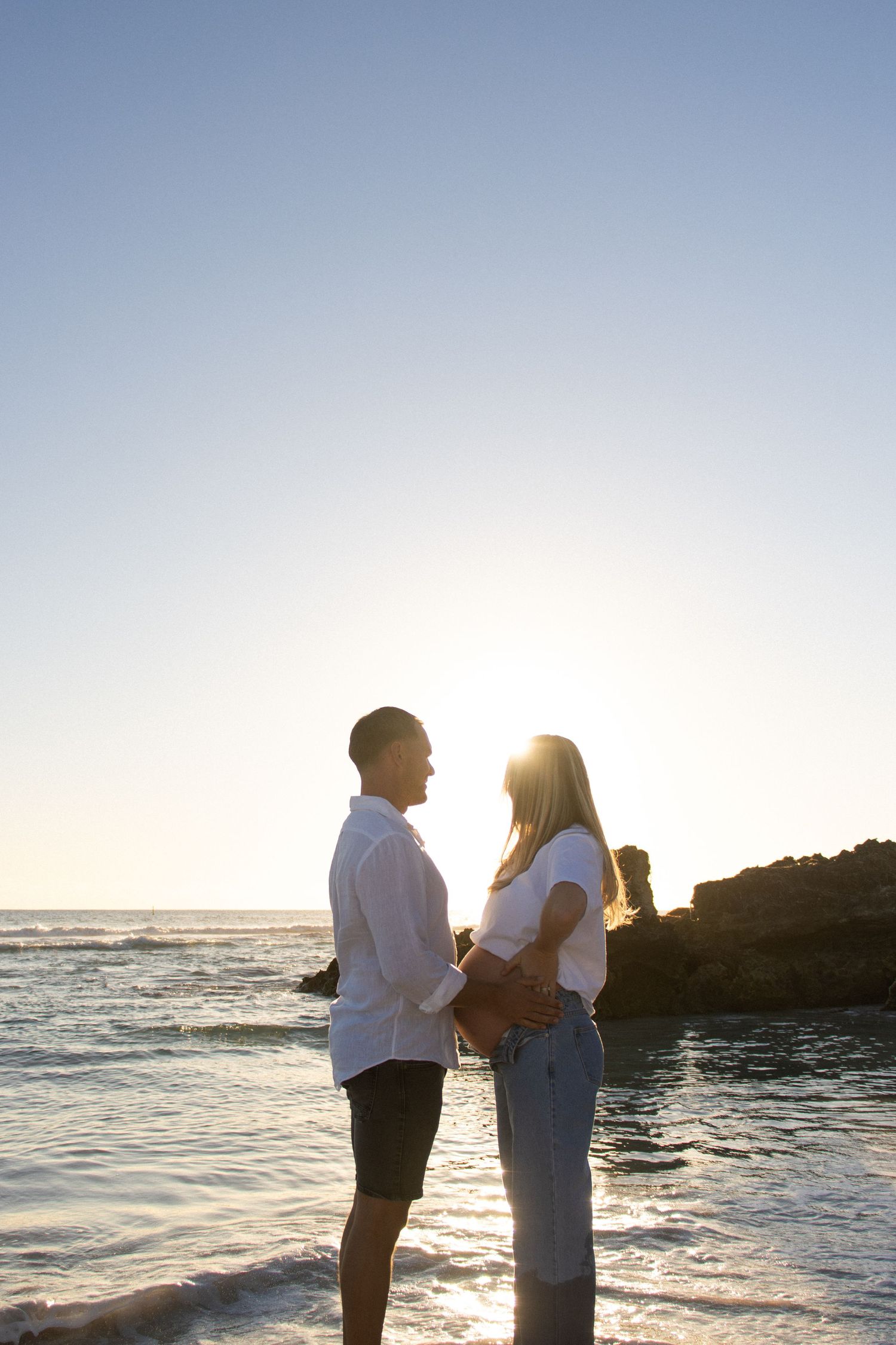 Couple celebrating their pregnancy announcement with natural, candid photos at a Perth beach during golden hour.