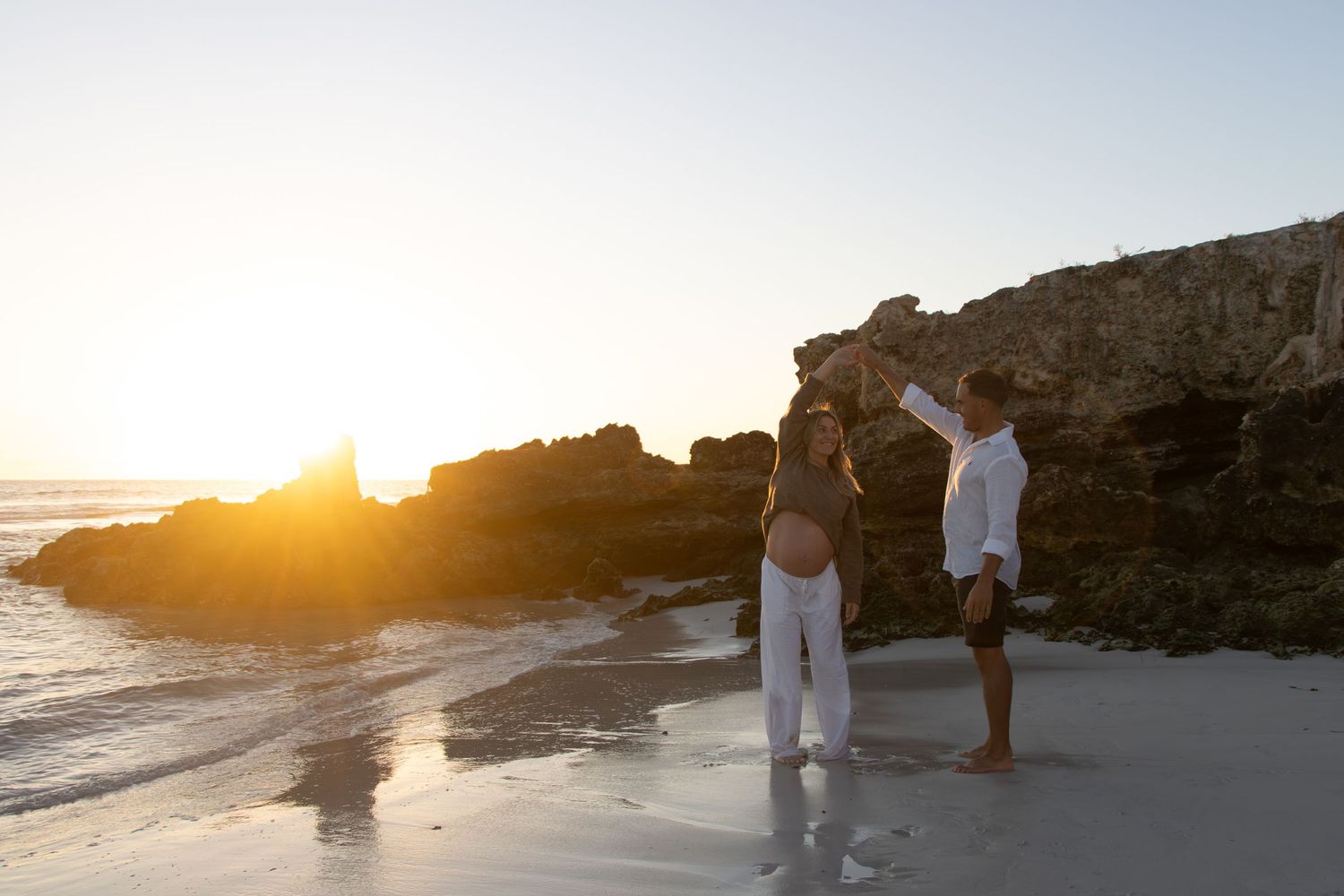 Mum-to-be walking along the beach with her partner during a natural outdoor maternity photography session in Perth at sunset.