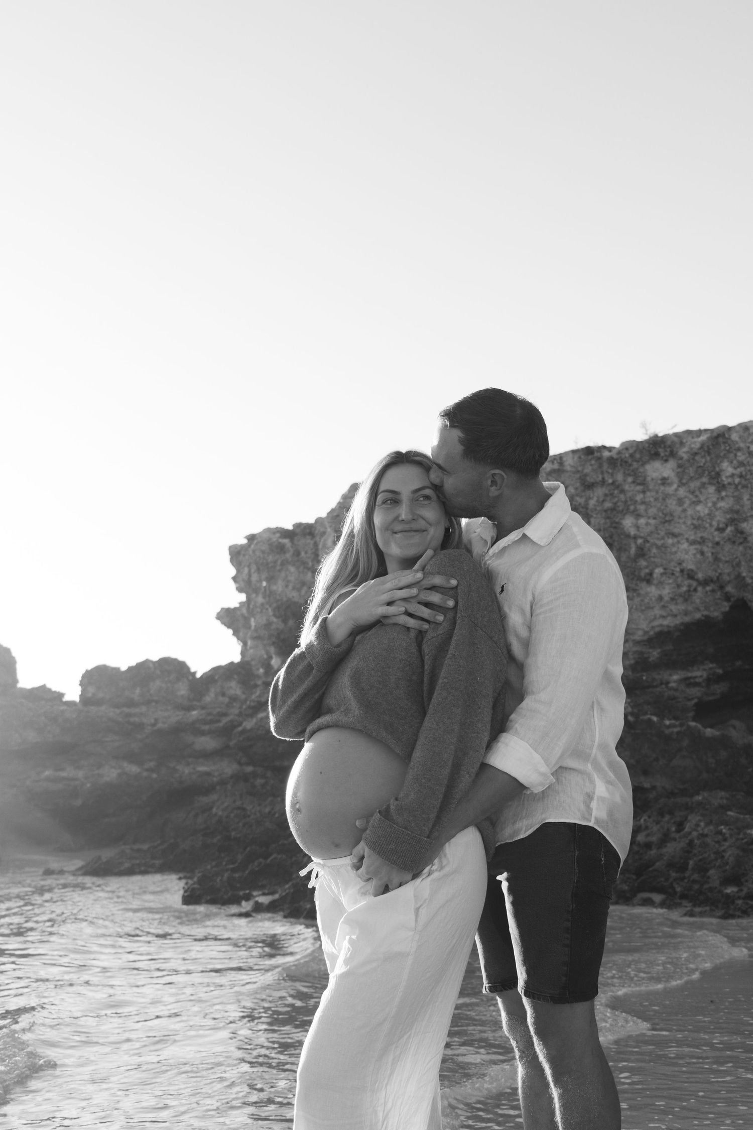Expecting mum holding her baby bump while smiling at her partner during a relaxed outdoor maternity session in Perth.