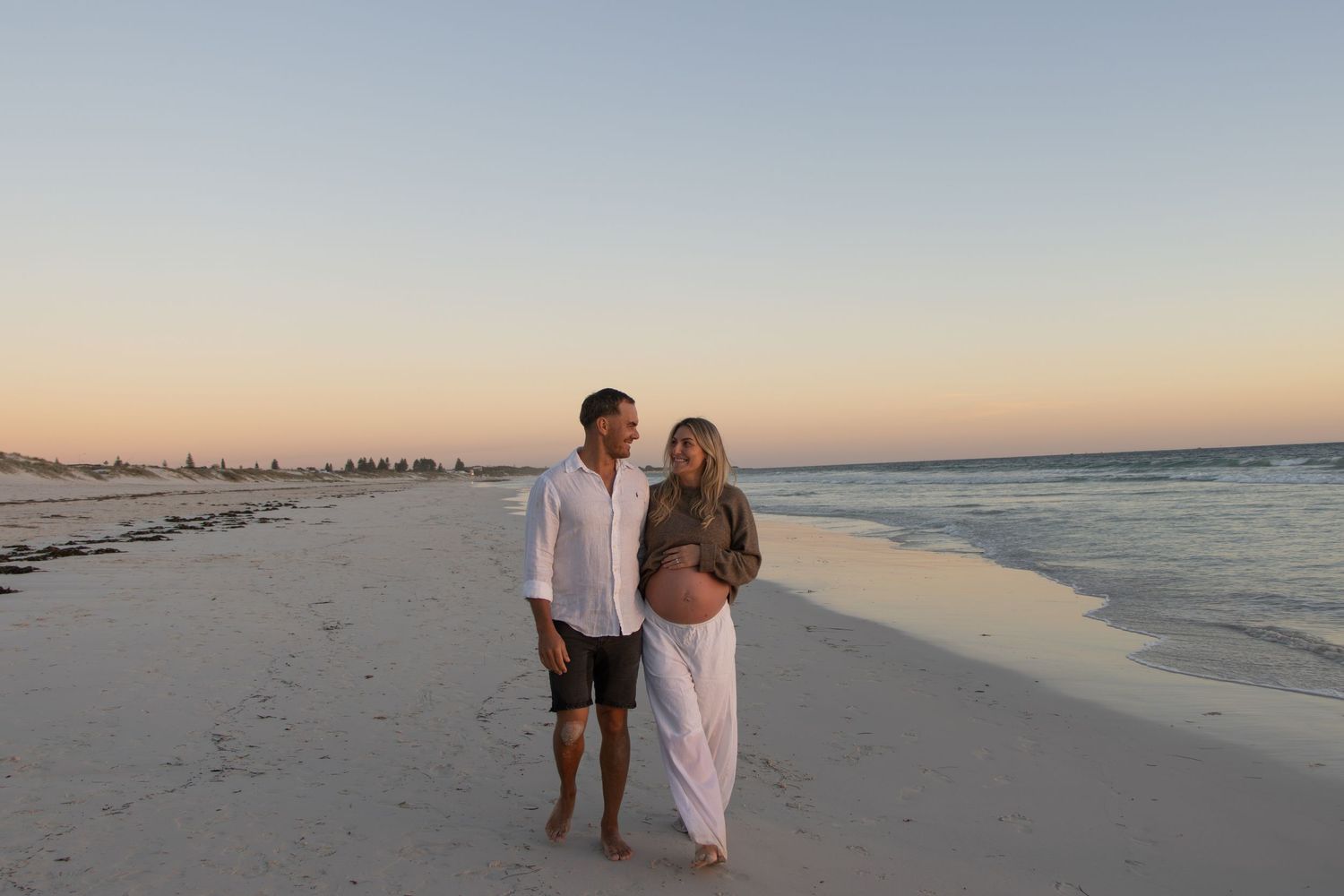 Couple celebrating their pregnancy announcement with natural, candid photos at a Perth beach during golden hour.