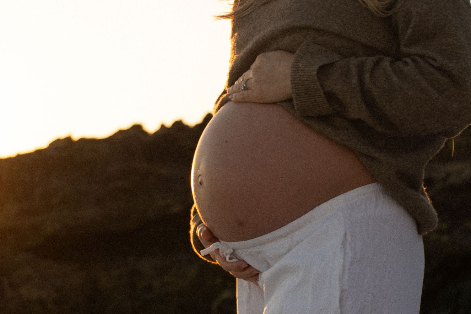 Couple celebrating their pregnancy announcement with natural, candid photos at a Perth beach during golden hour.