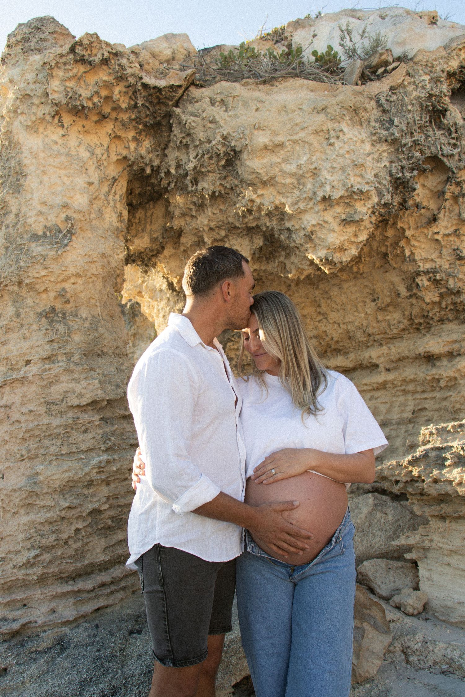 Couple celebrating their pregnancy announcement with natural, candid photos at a Perth beach during golden hour.
