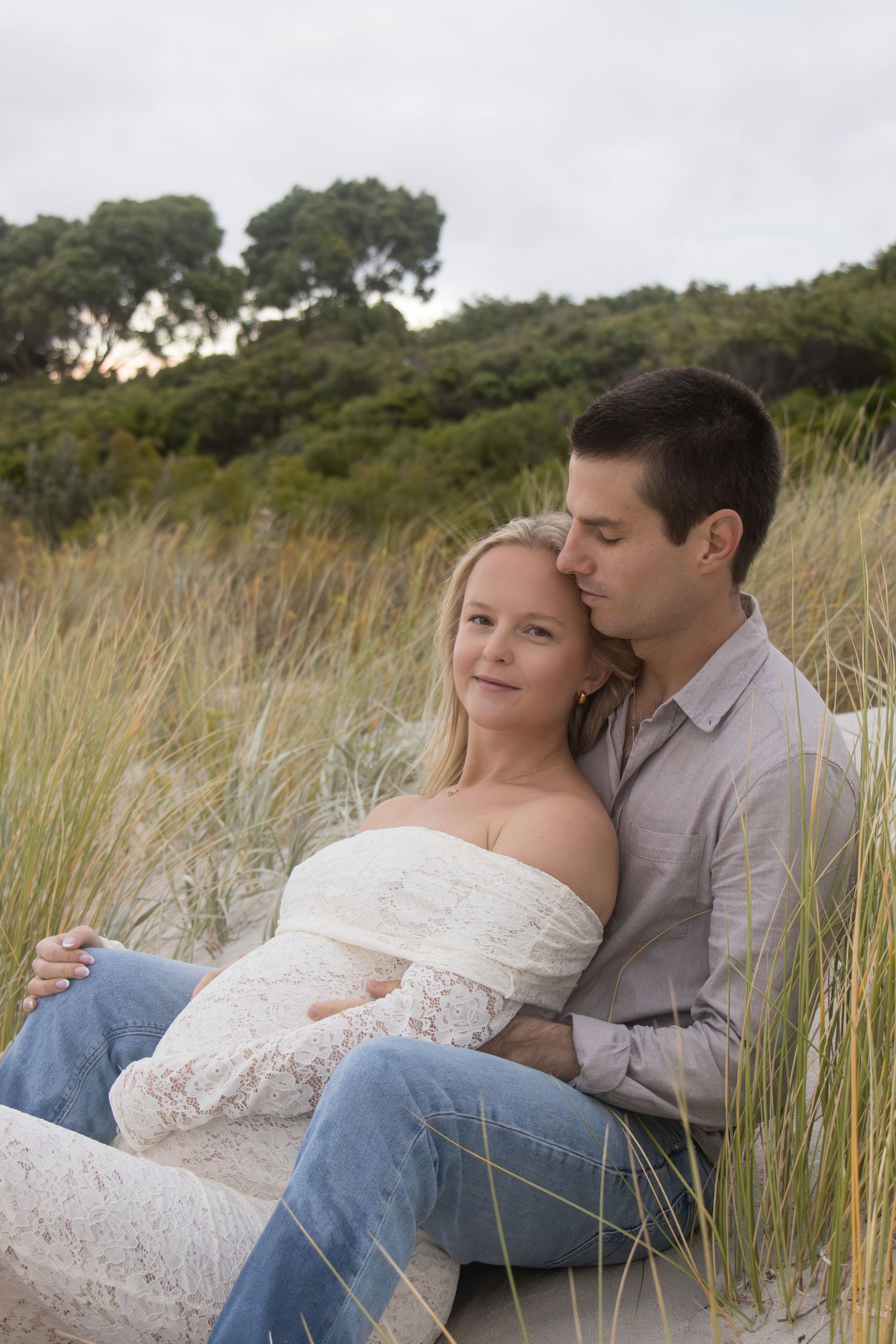 Expecting mum holding her baby bump while smiling at the camera during a relaxed outdoor maternity session in Albany.