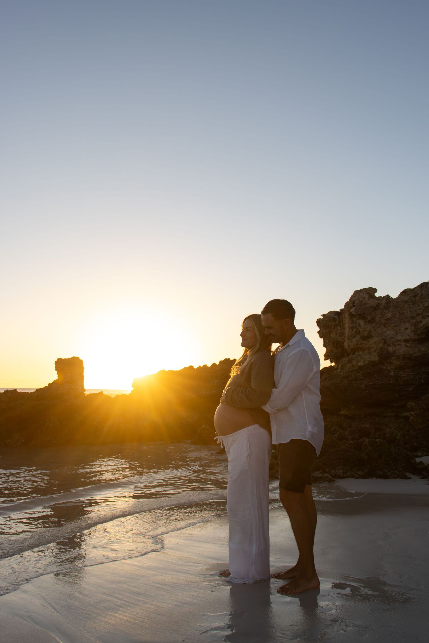 Mum-to-be walking along the beach with her partner during a natural outdoor maternity photography session in Perth at sunset.