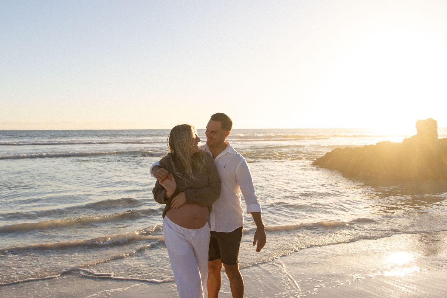 Couple celebrating their pregnancy announcement with natural, candid photos at a Perth beach during golden hour.