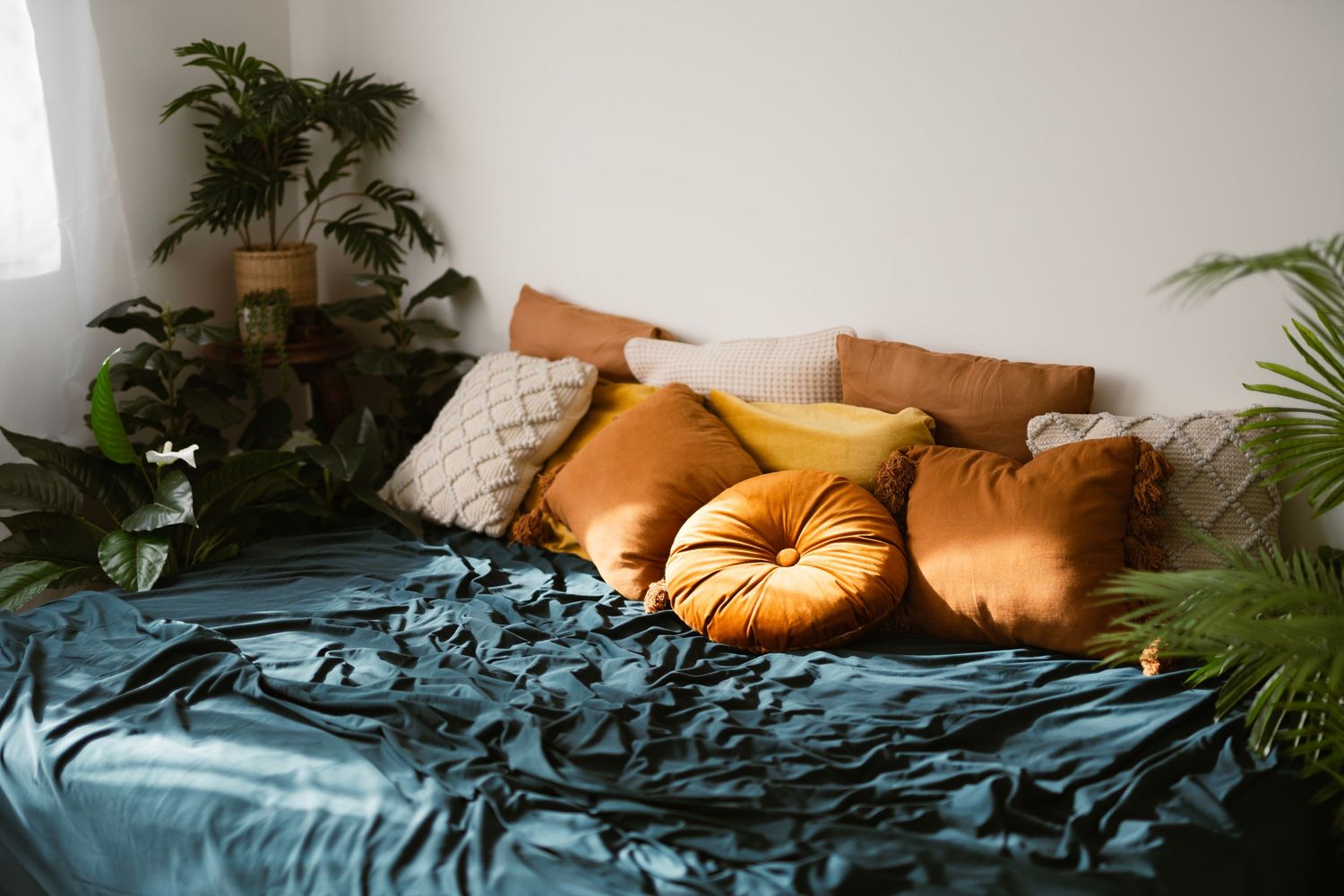 Melbourne Boudoir Studio's space. A cozy bed with teal velvet bedding and rust orange pillows, accented by tropical plants in the corners.