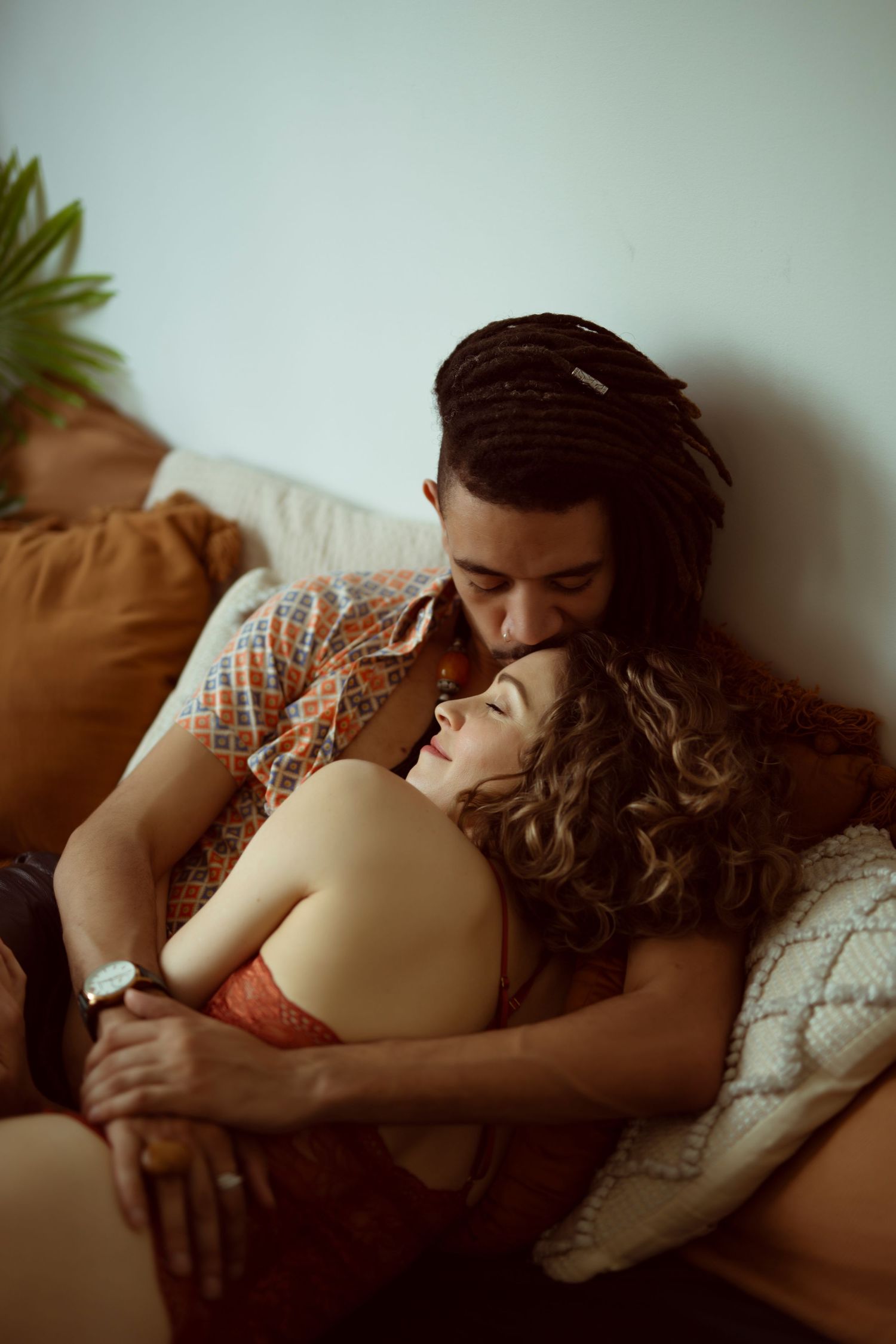 A couple shares an intimate moment while resting together on a couch in warm lighting.