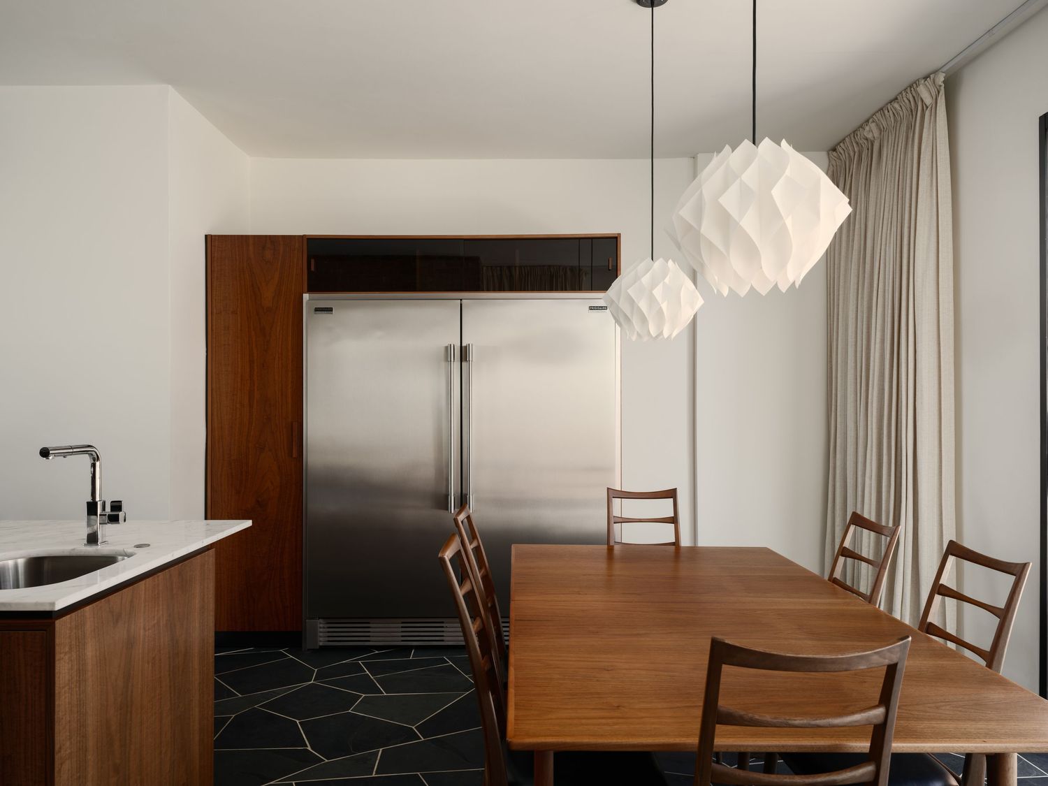 Dining area with sculptural pendant lights, custom walnut cabinetry and stainless kitchen backdrop in renovated Liepman Residence