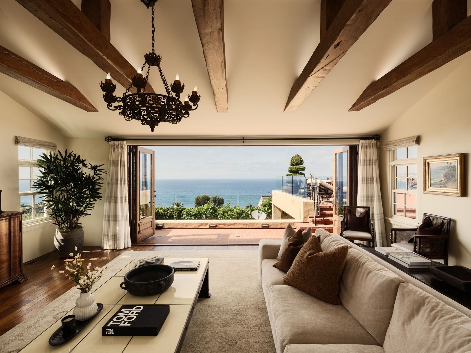 Ocean-view living room at 7757 Whitefield with exposed beams, iron chandelier, and French doors opening to terrace.