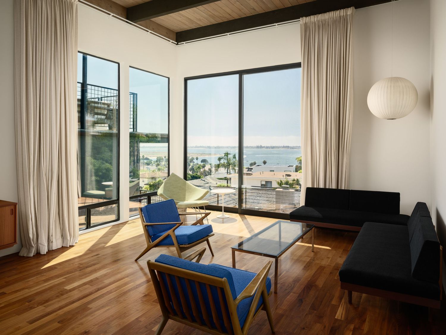 Liepman Residence living room with ocean and bay views through floor-to-ceiling windows, modern seating and warm wood floors