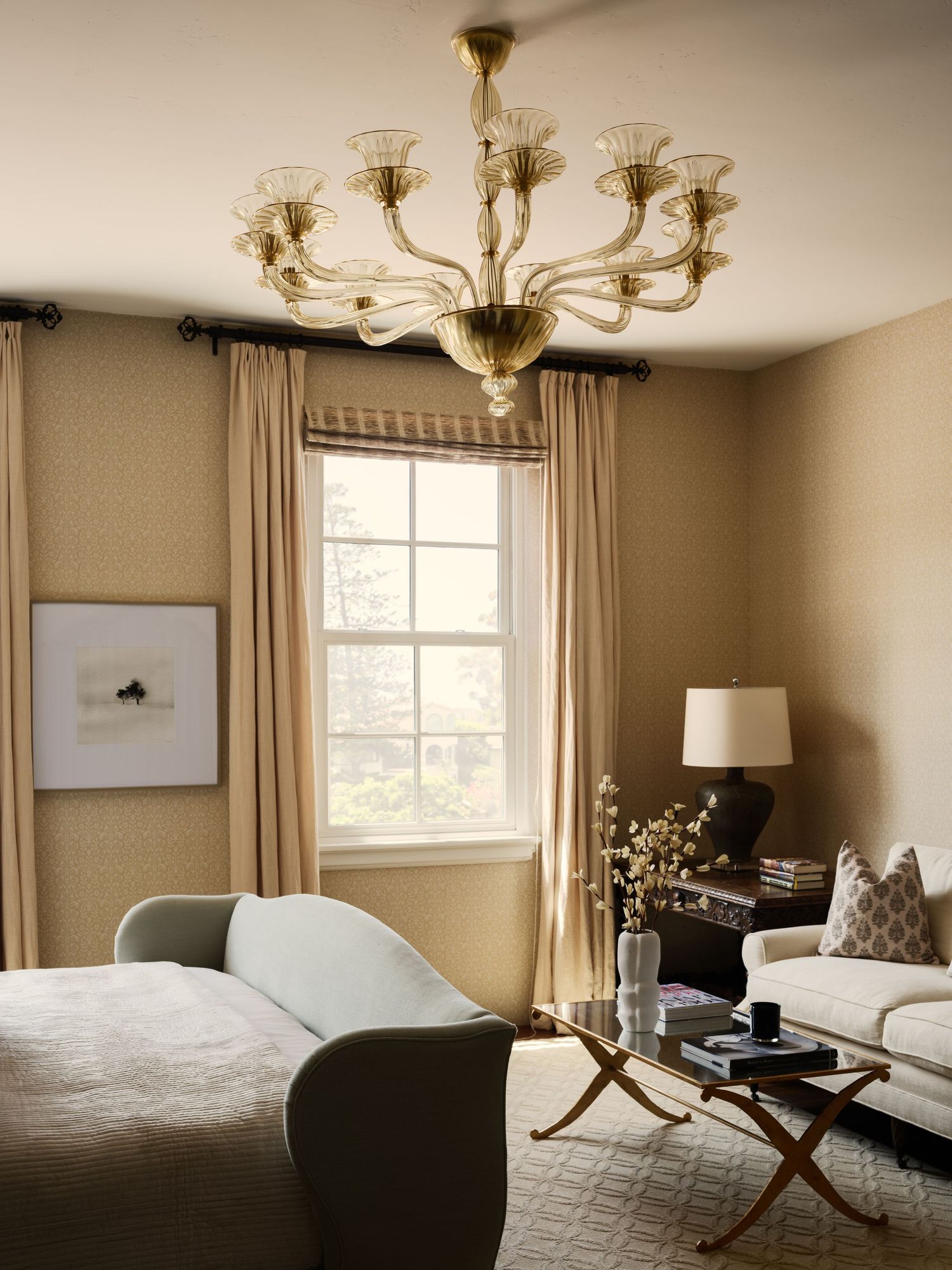 Guest bedroom sitting area at 7757 Whitefield with sculptural chaise, soft textiles, window light, and vintage glass chandelier.