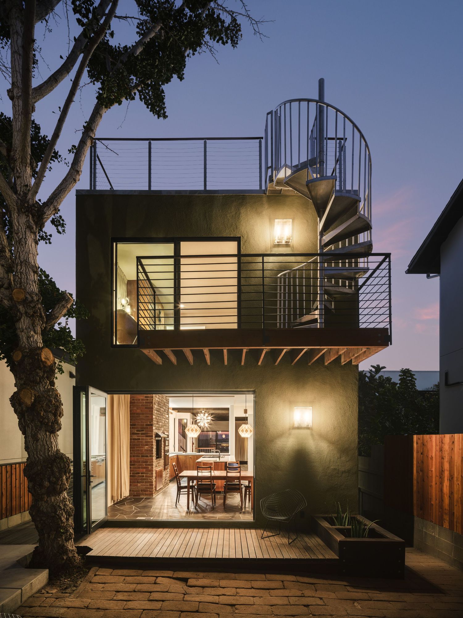 Dusk exterior of the Liepman Residence by Bruce Dammann, with rooftop deck, redwood balconies and warm interior glow by Luca Prodi