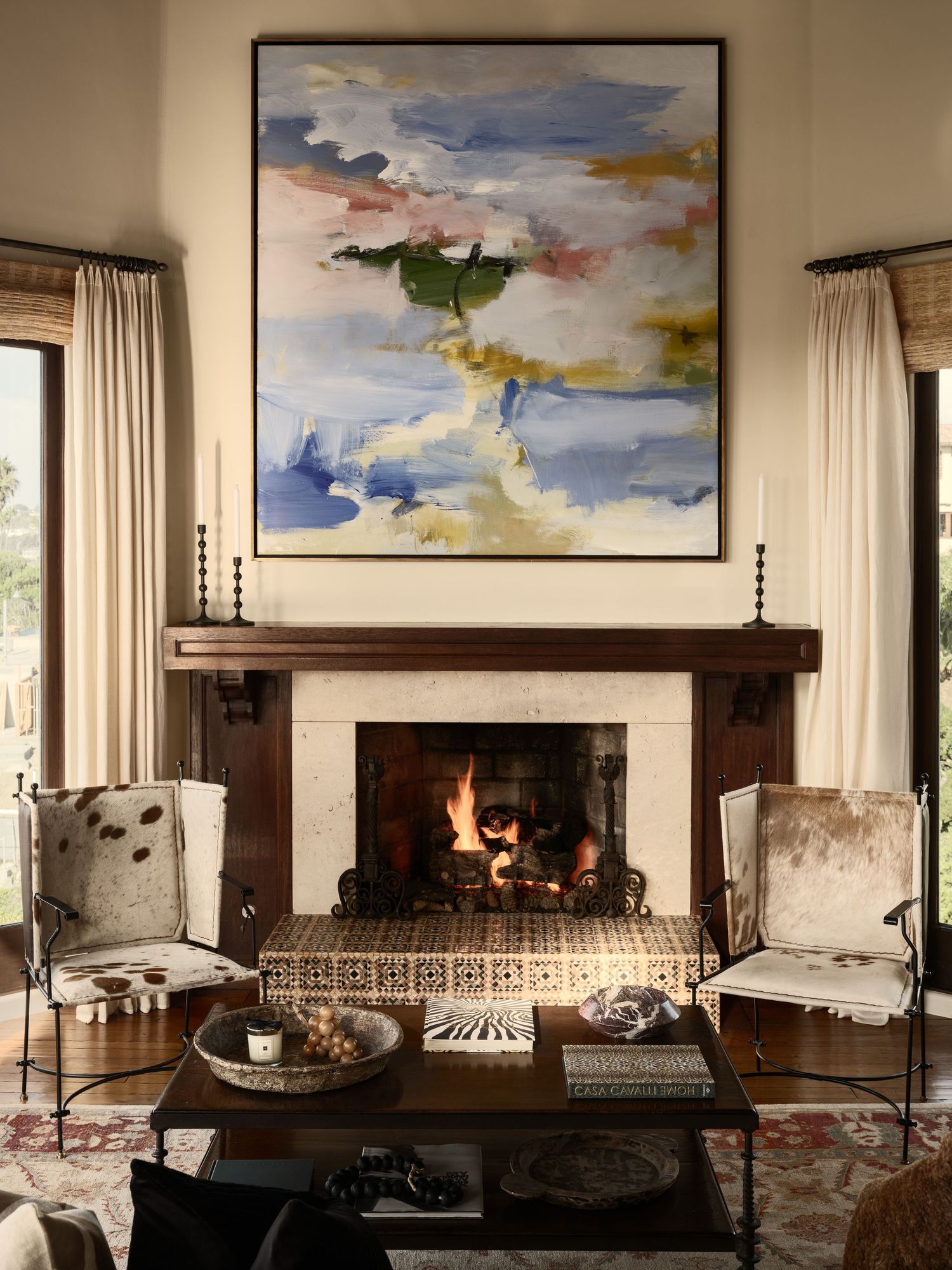 Staged living room at 7757 Whitefield featuring a lit fireplace, patterned tile hearth, oversized abstract art, and paired lounge chairs.