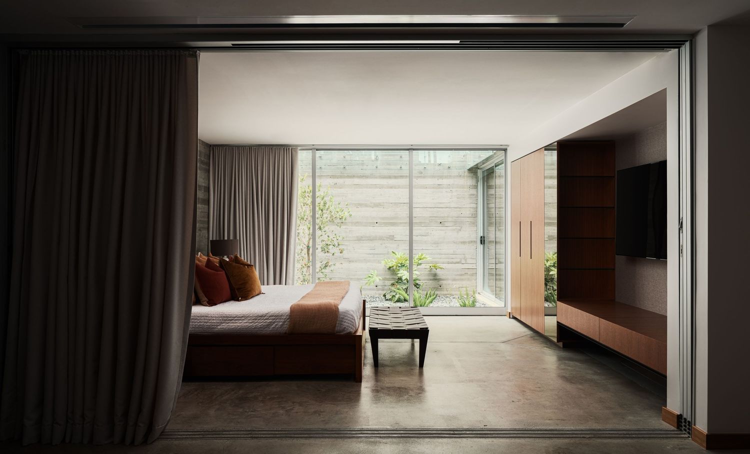 Primary bedroom at 7003 Fay Avenue opening to a private courtyard, featuring minimalist detailing, concrete floors, and warm wood cabinetry.