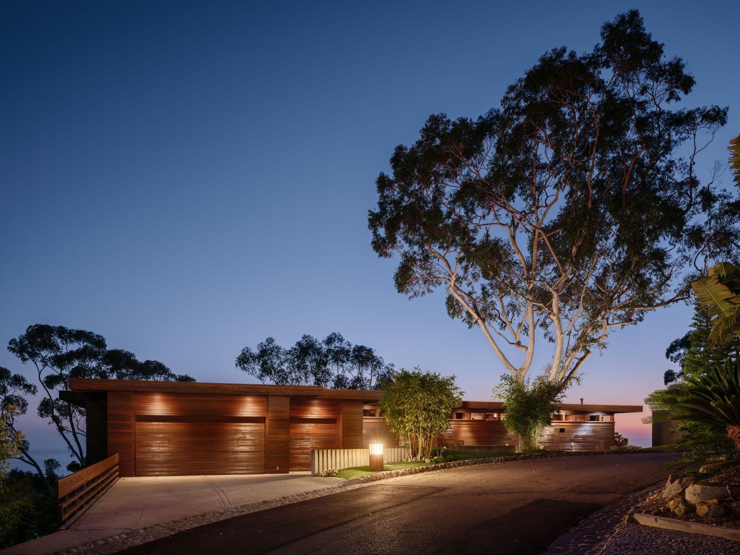 Twilight street view of 7226 Romero in La Jolla, a midcentury luxury home by Frederick Liebhardt with warm wood siding and coastal setting.