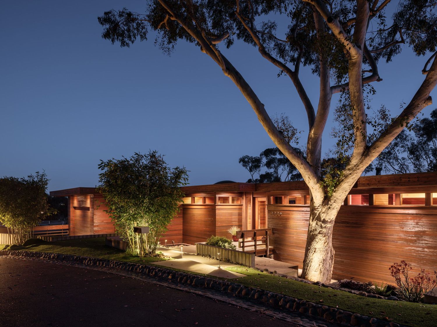 Dusk exterior of 7226 Romero Drive in La Jolla, a cedar clad midcentury home by Frederick Liebhardt with soft path lighting.