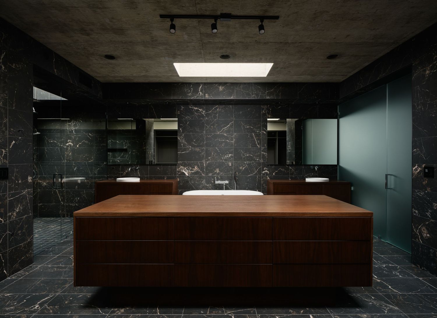 Arista Residence primary bathroom interior by Matthew Segal, dark stone walls, custom wood vanity, skylight, and minimalist design.