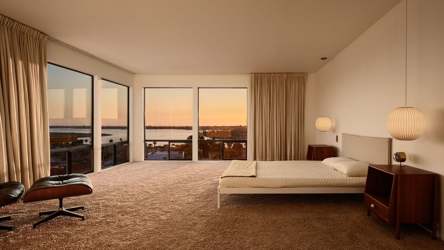 Primary bedroom with sunset city-and-bay view, neutral finishes and lounge chair in the Liepman Residence, Bay Park San Diego