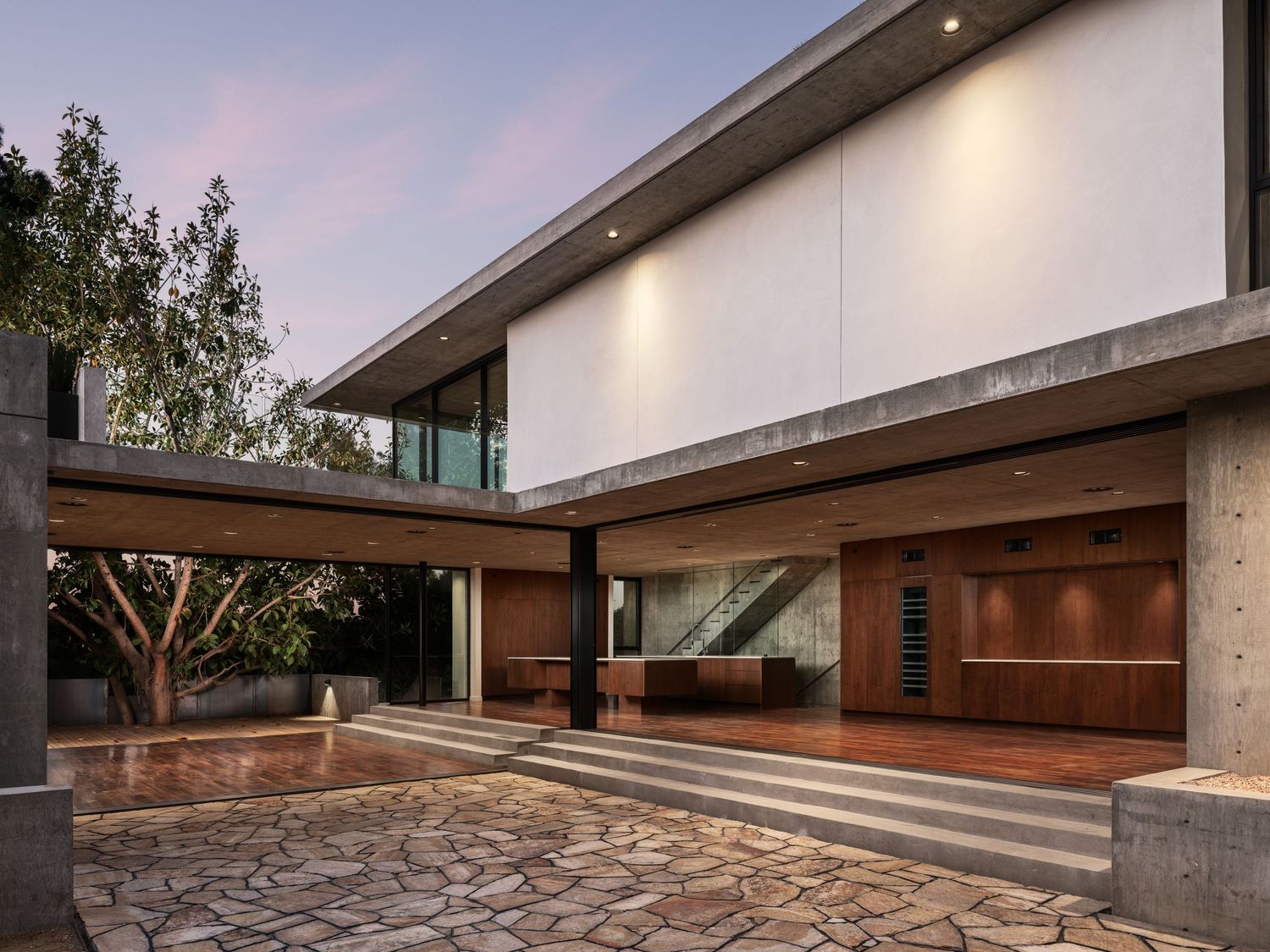 Arista Residence exterior courtyard by Matthew Segal, modern concrete and wood architecture with cantilevered roof at dusk.