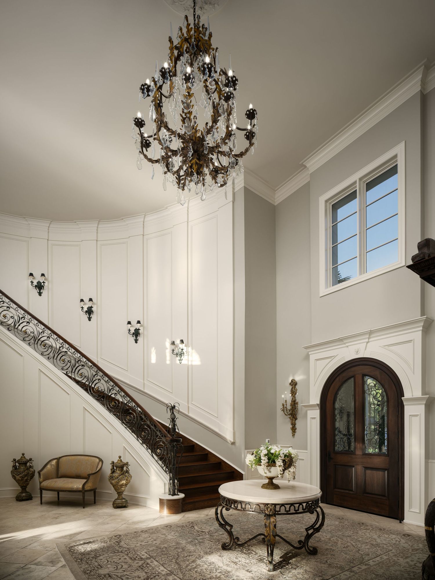 Grand staircase foyer with ornate iron railing, chandelier, and custom millwork, photographed to highlight luxury architectural design.