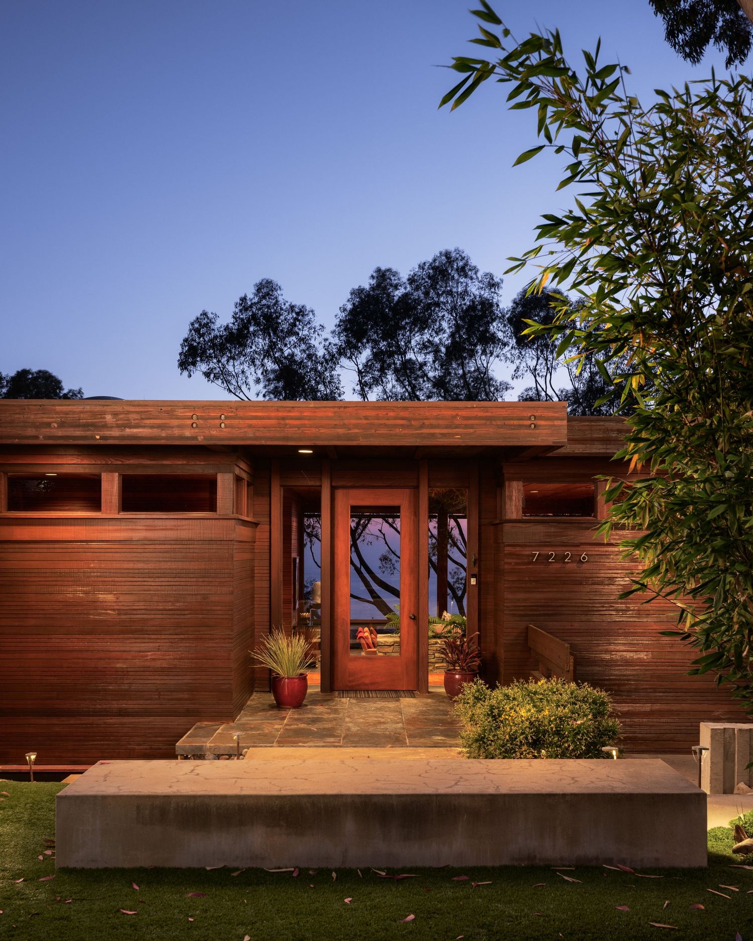 Twilight view of the front entry at 7226 Romero, a midcentury luxury home in La Jolla with cedar siding and warm architectural lighting.