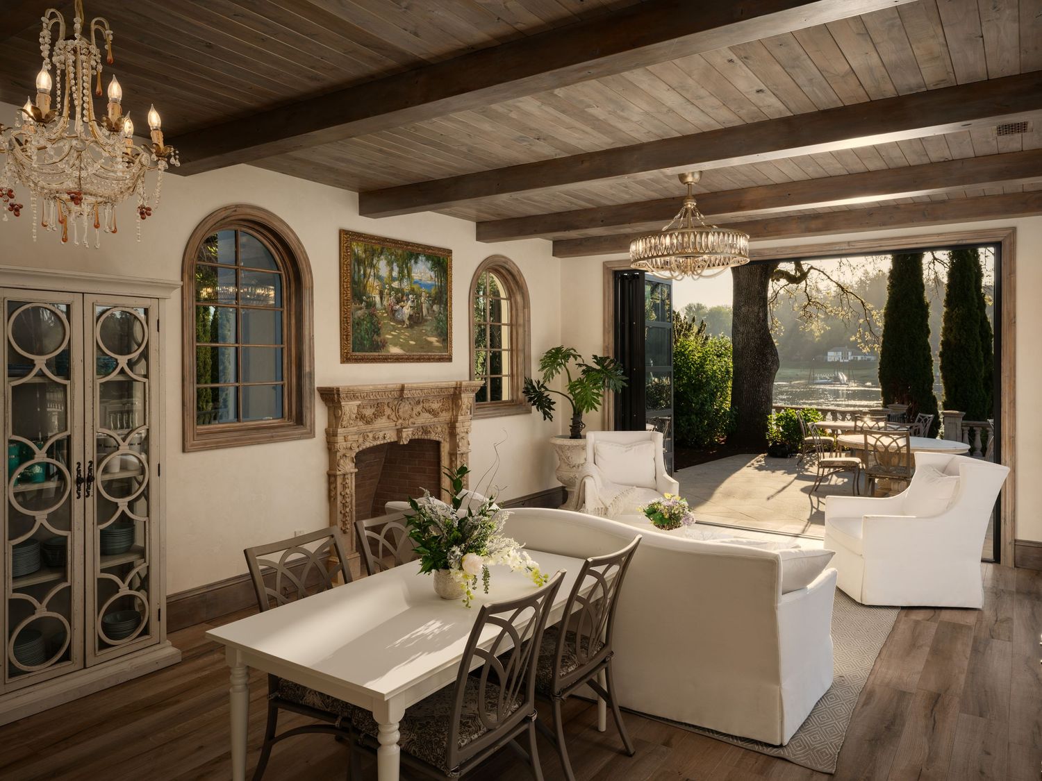 Covered outdoor living space at the Fielding House featuring wood beams, fireplace, chandeliers, and lounge seating overlooking the gardens.