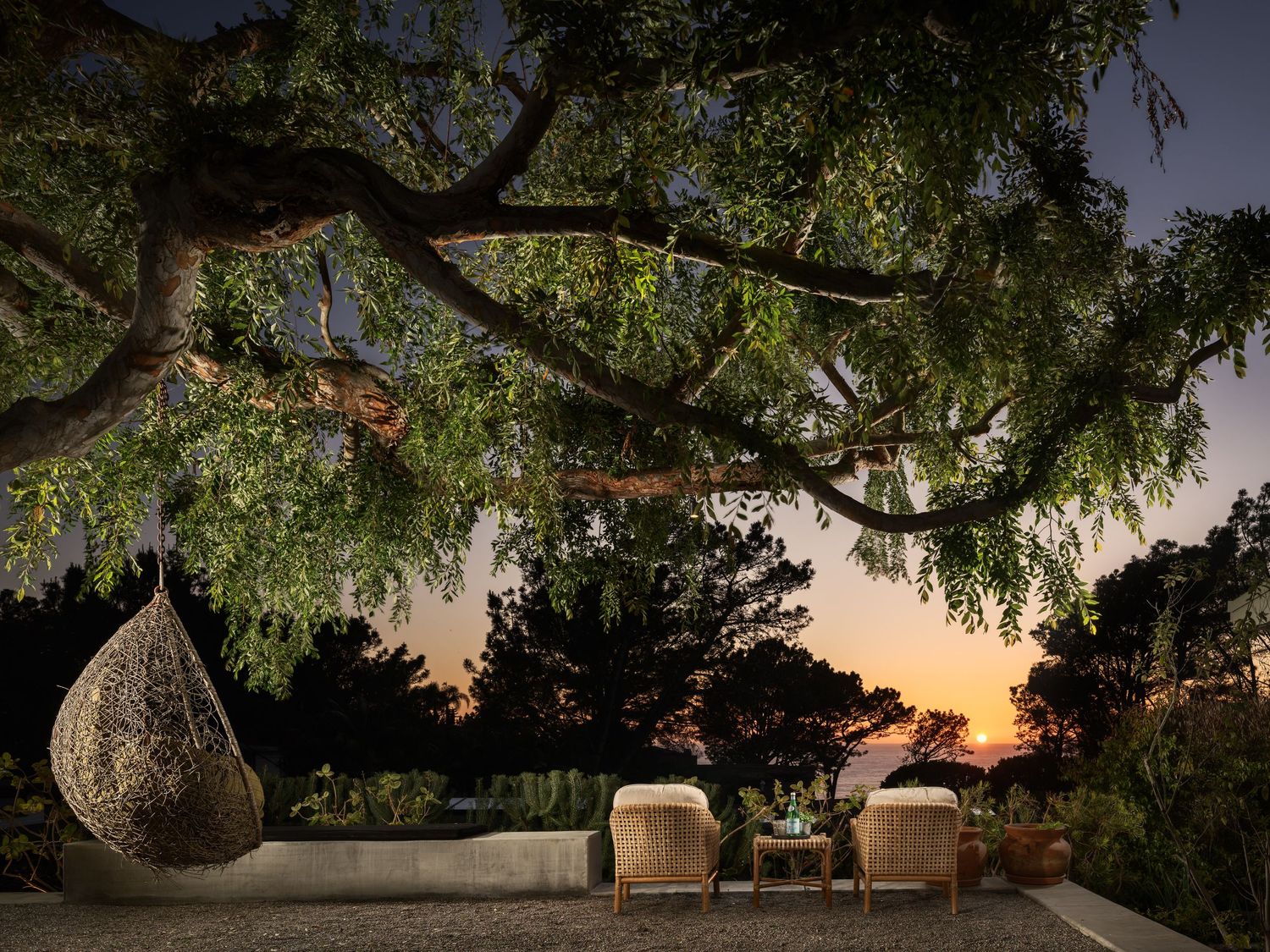 Twilight outdoor living space in Del Mar with ocean sunset views, lounge seating, hanging chair, and tree canopy in a luxury coastal setting