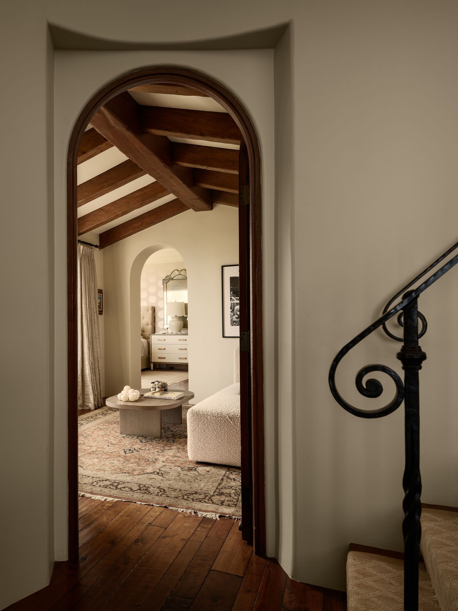 Arched doorway and wrought-iron stair detail at 7757 Whitefield, framing a Spanish-style sitting room with exposed beams and wood floors.