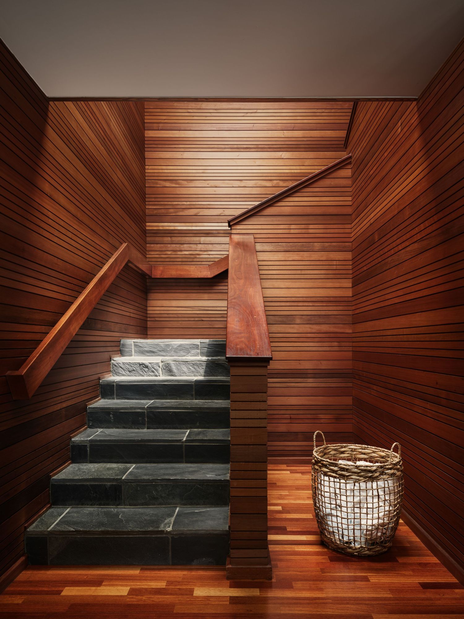 Midcentury staircase at 7226 Romero with rich wood paneling and stone steps, interior design photography san diego.