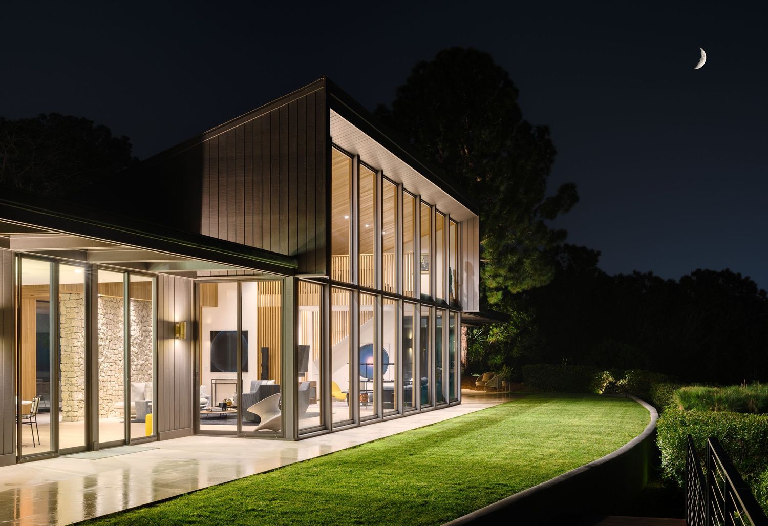 Night exterior of 7404 Hillside Drive showcasing a refined modern façade, expansive glazing, and architectural lighting.