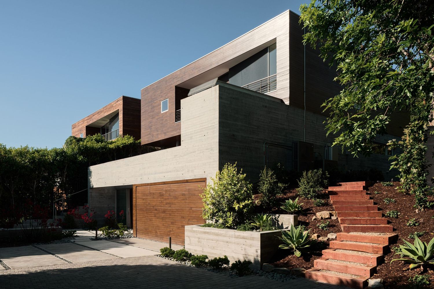 Angled exterior view of 7003 Fay Avenue showing layered concrete, wood cladding, and stepped approach in a modern coastal setting.