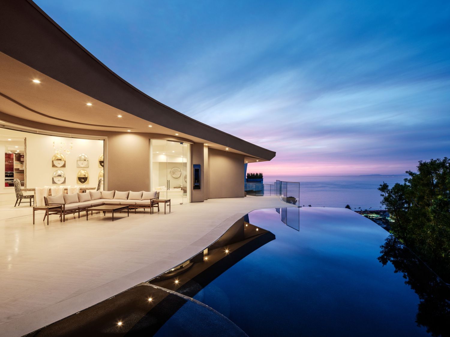 Twilight view of a curved La Jolla hillside residence with ocean-view terrace and infinity-edge pool reflecting the dusk sky.