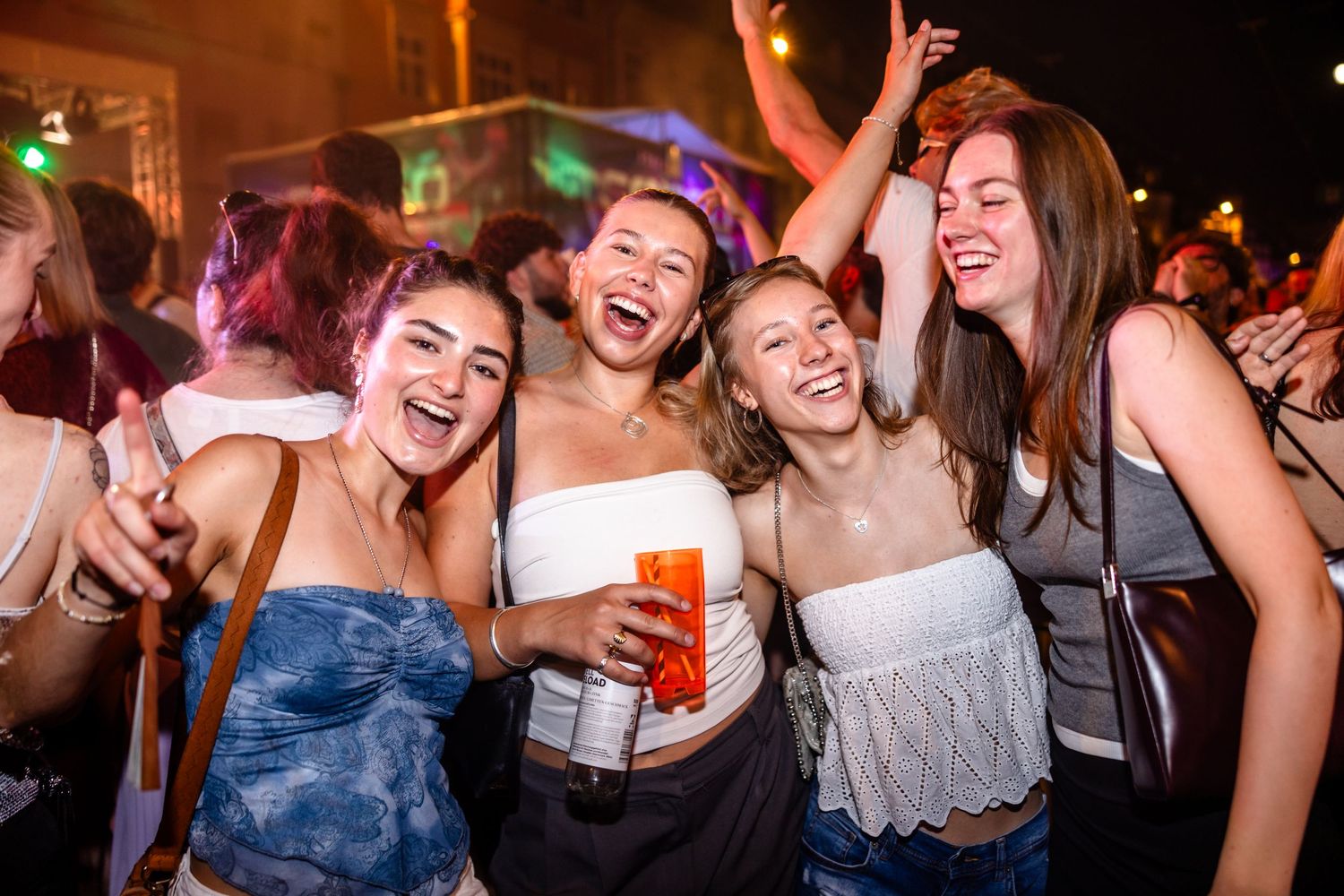 Four young women laughing and dancing together at an outdoor nighttime party event.