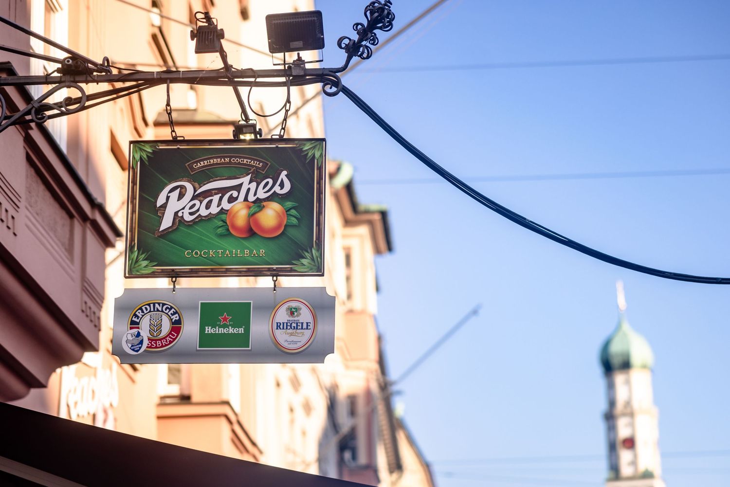 Peaches bar sign with Heineken logo displayed on a building facade against a clear blue sky.