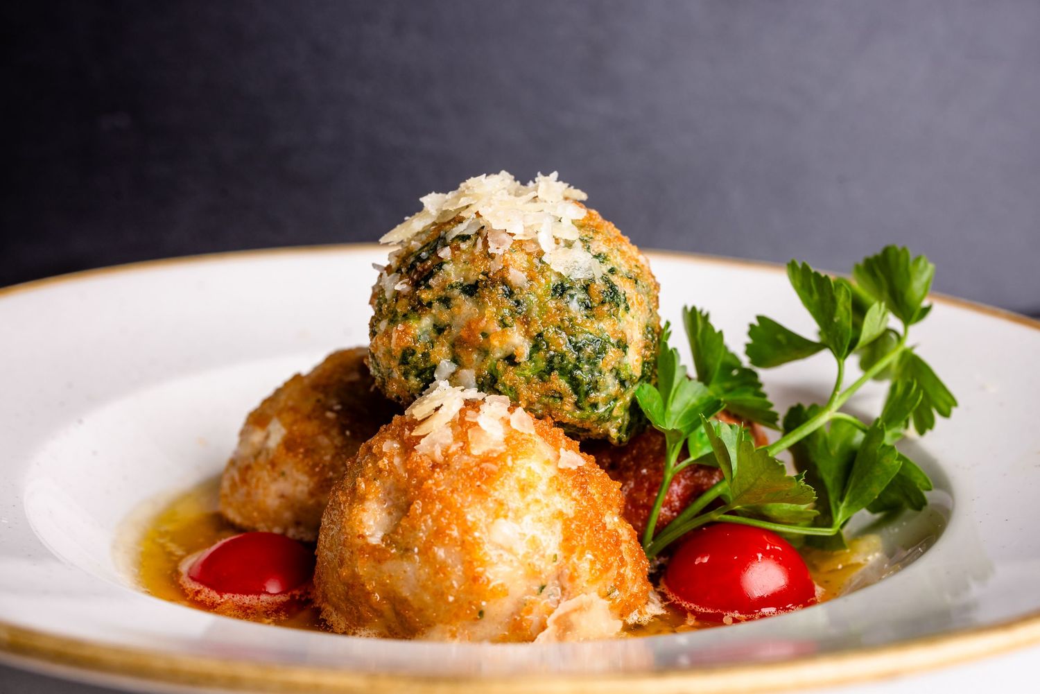 Golden arancini rice balls topped with herbs and Parmesan on a white plate with cherry tomatoes and fresh parsley.