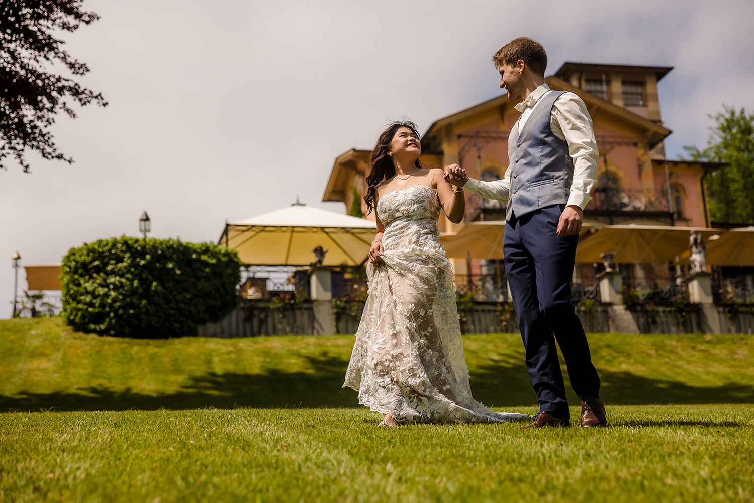 A couple in wedding attire dances together on a grassy hillside during a romantic outdoor celebration.