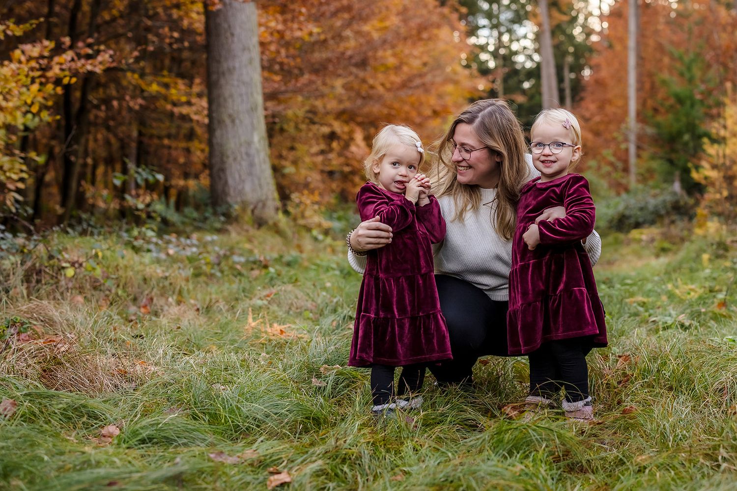 A family sits together on a wooden bench surrounded by vibrant autumn foliage in a forest setting.