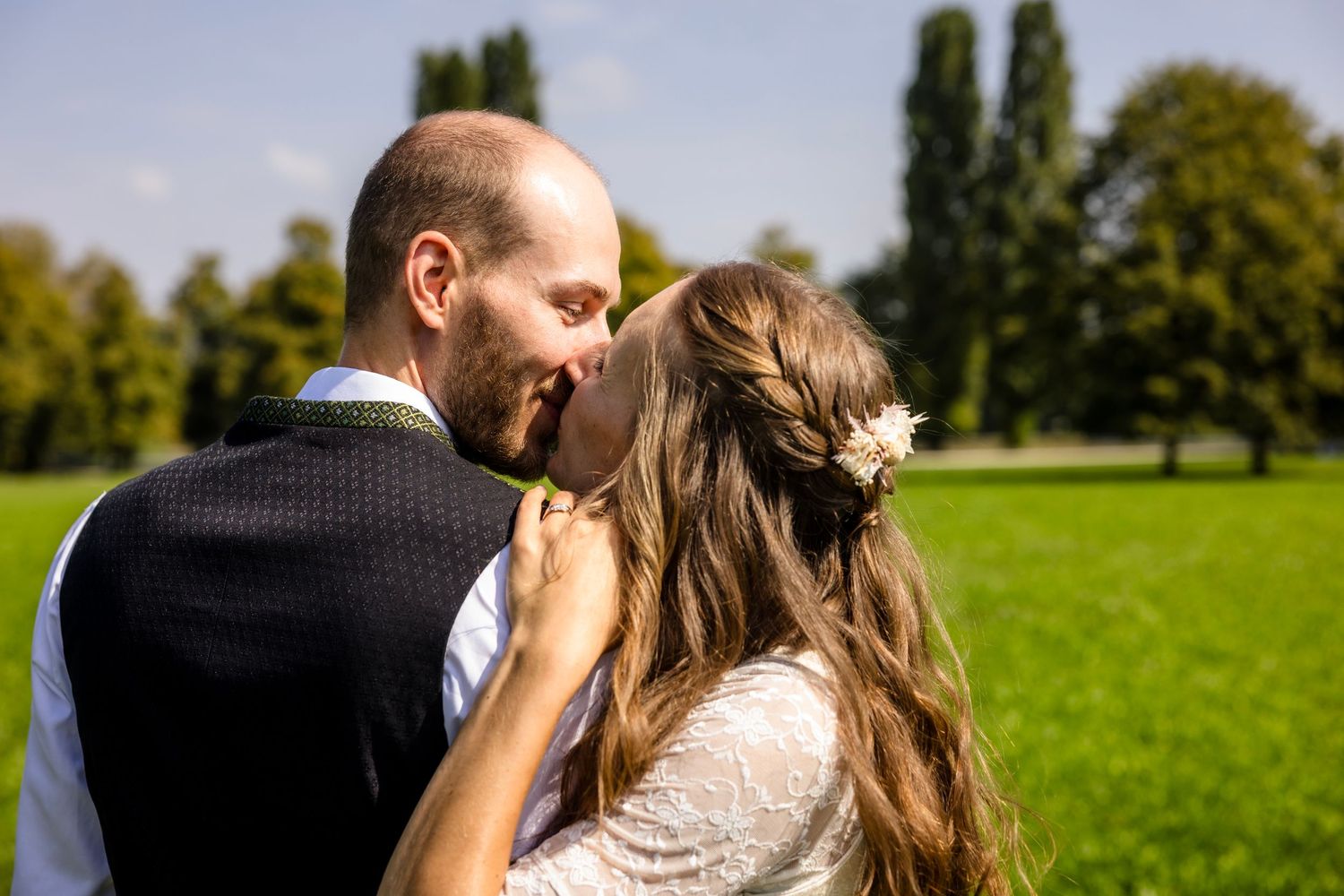 Bride and groom sharing a romantic moment outdoors on their wedding day in a lush green park setting.