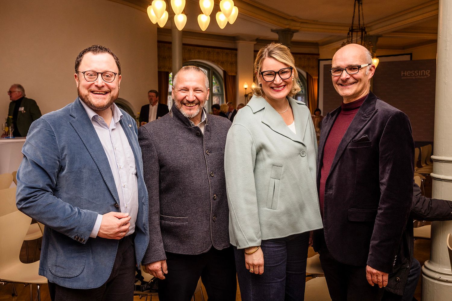 Business professionals gathered for indoor networking event under warm chandelier lighting.