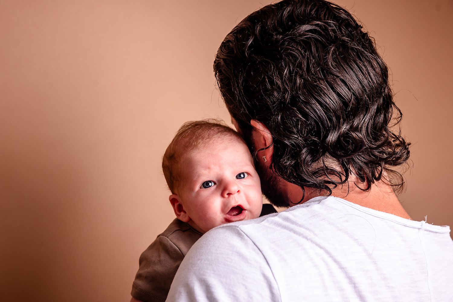 A tender moment captured between parent and baby in a warm sepia-toned portrait series.