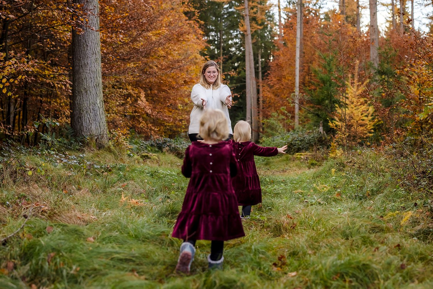 A couple walks hand in hand through a vibrant autumn forest with golden leaves and tall trees.