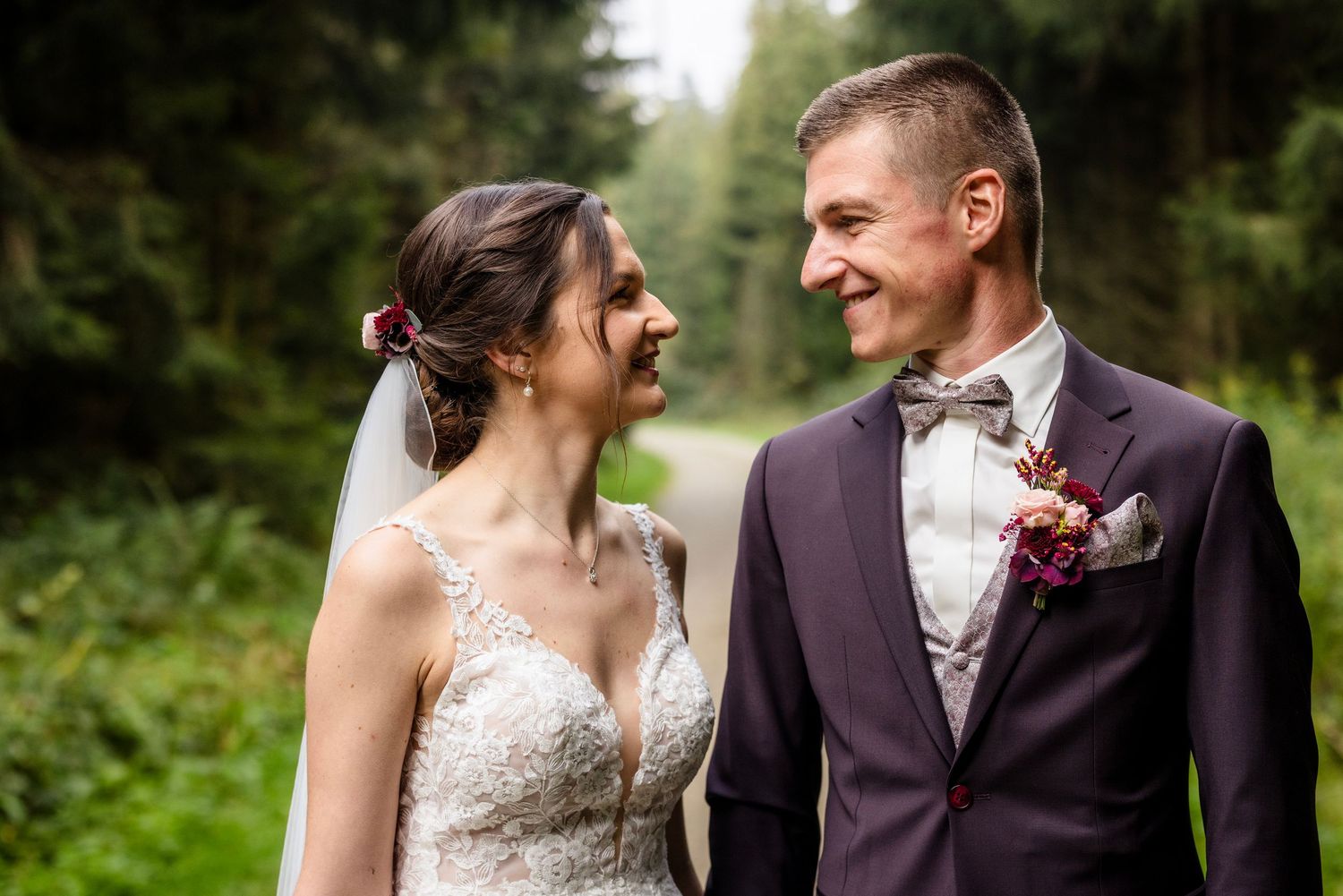 Happy bride and groom smiling at each other outdoors in a lush forest setting on their wedding day.