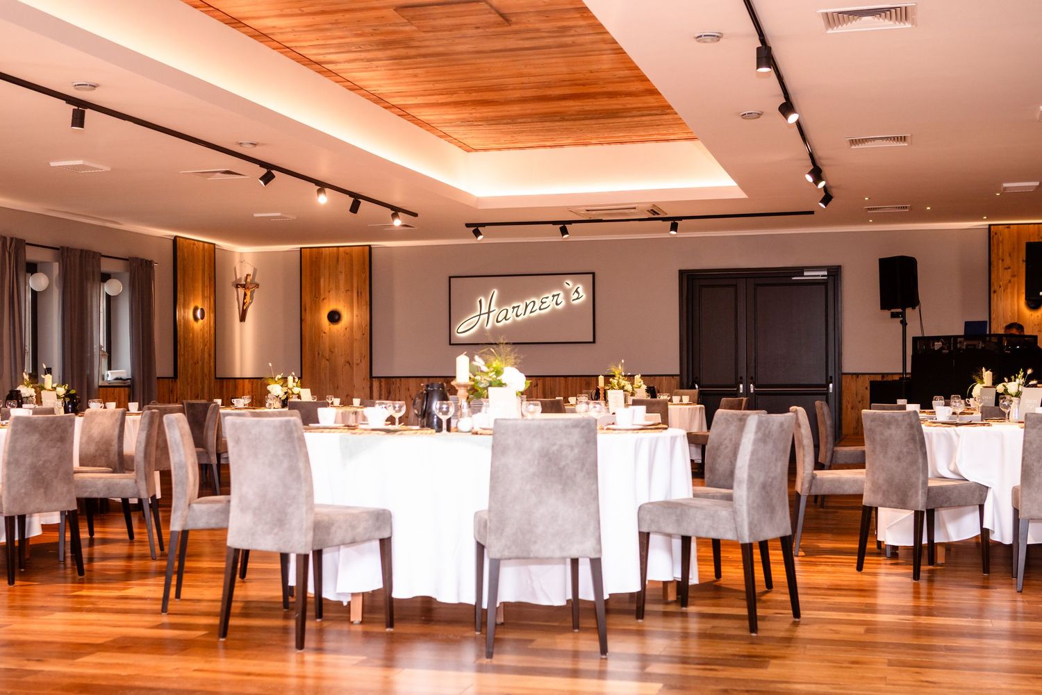 Elegant banquet hall with white tablecloths, wood paneled ceiling, and warm lighting creates an upscale dining atmosphere.
