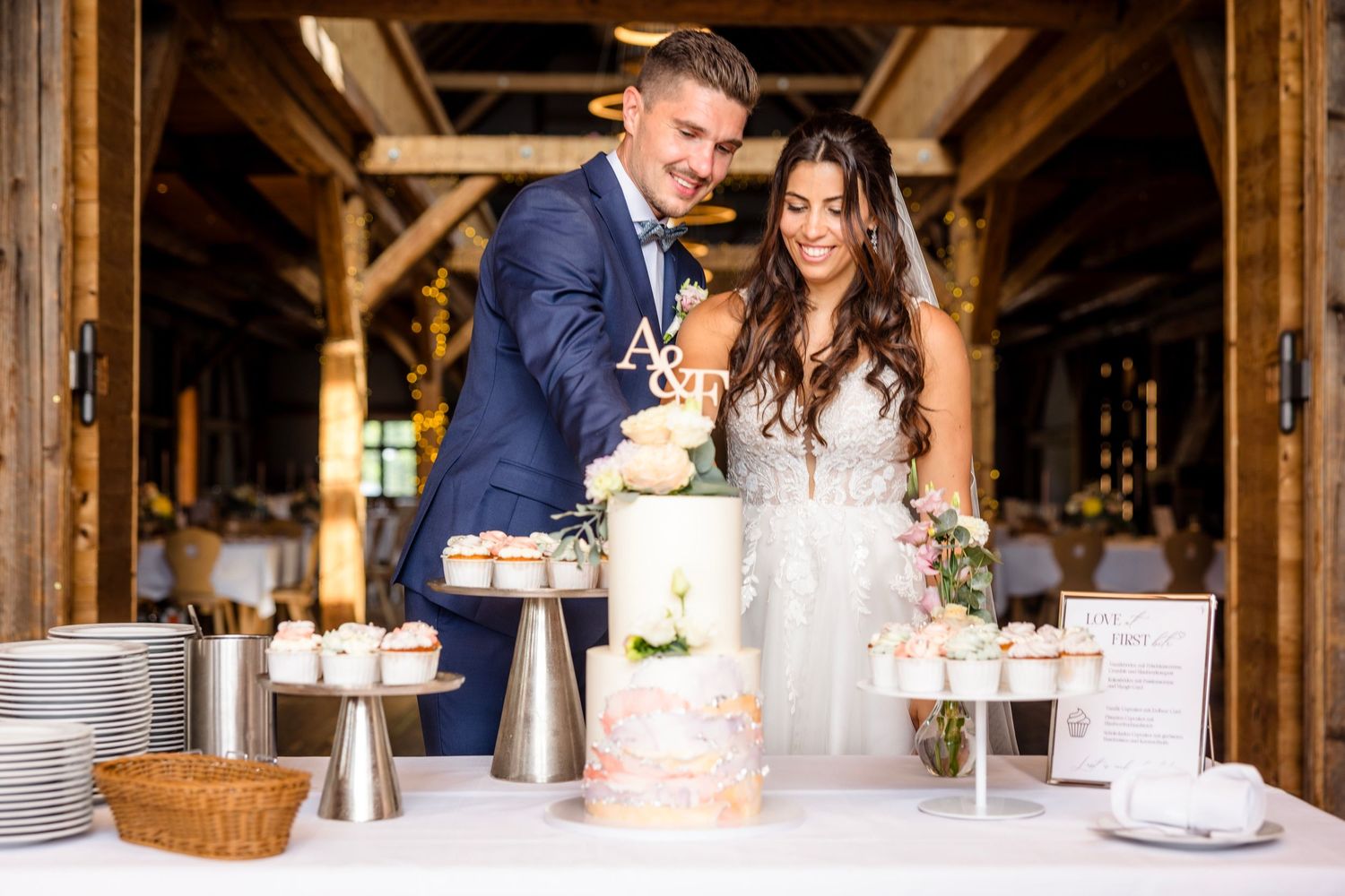 A couple shares a tender moment during their rustic barn wedding reception with warm lighting and table settings.
